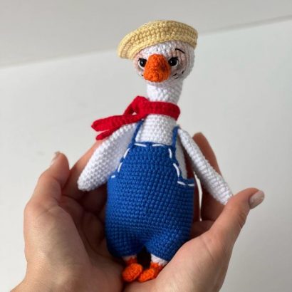 В’язана іграшка біле гусенятко в комбінезоні з кепкою